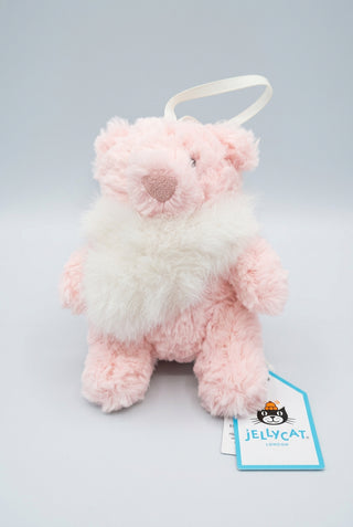 A small plush bear keychain in pale pink and white faux fur, with a white hanging loop and a visible Jellycat tag, photographed on a wooden surface against a dark background.