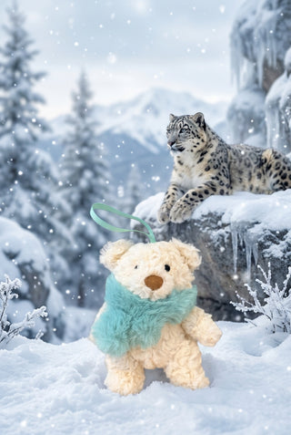 A small cream-colored plush teddy bear keychain or charm with a fuzzy mint green scarf and a matching mint green hanging loop, resting on a light wood tabletop.
